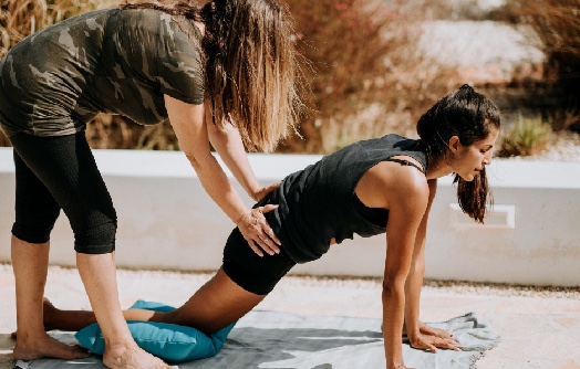 Femme dans la position du croissant bas les mains au sol avec quelqu'un qui la corrige