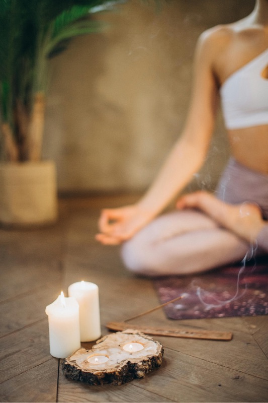 femme en méditation en arrière plan, au premier plan, des bougies et de l'encens